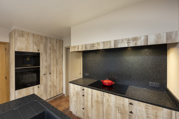 Kastenwand in lichte houtkleur met inductiekookplaat en dampkap in luifel met houten balk. Zwarte knopgreepjes.